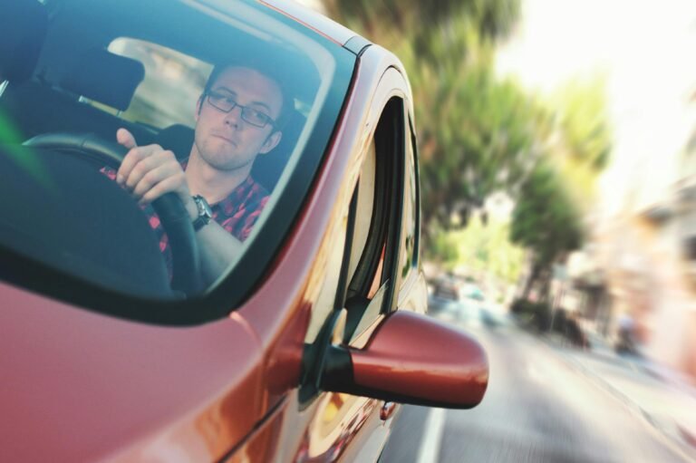 Enquiries 22 A man driving fast through a city street in a red car, showcasing motion and focus.