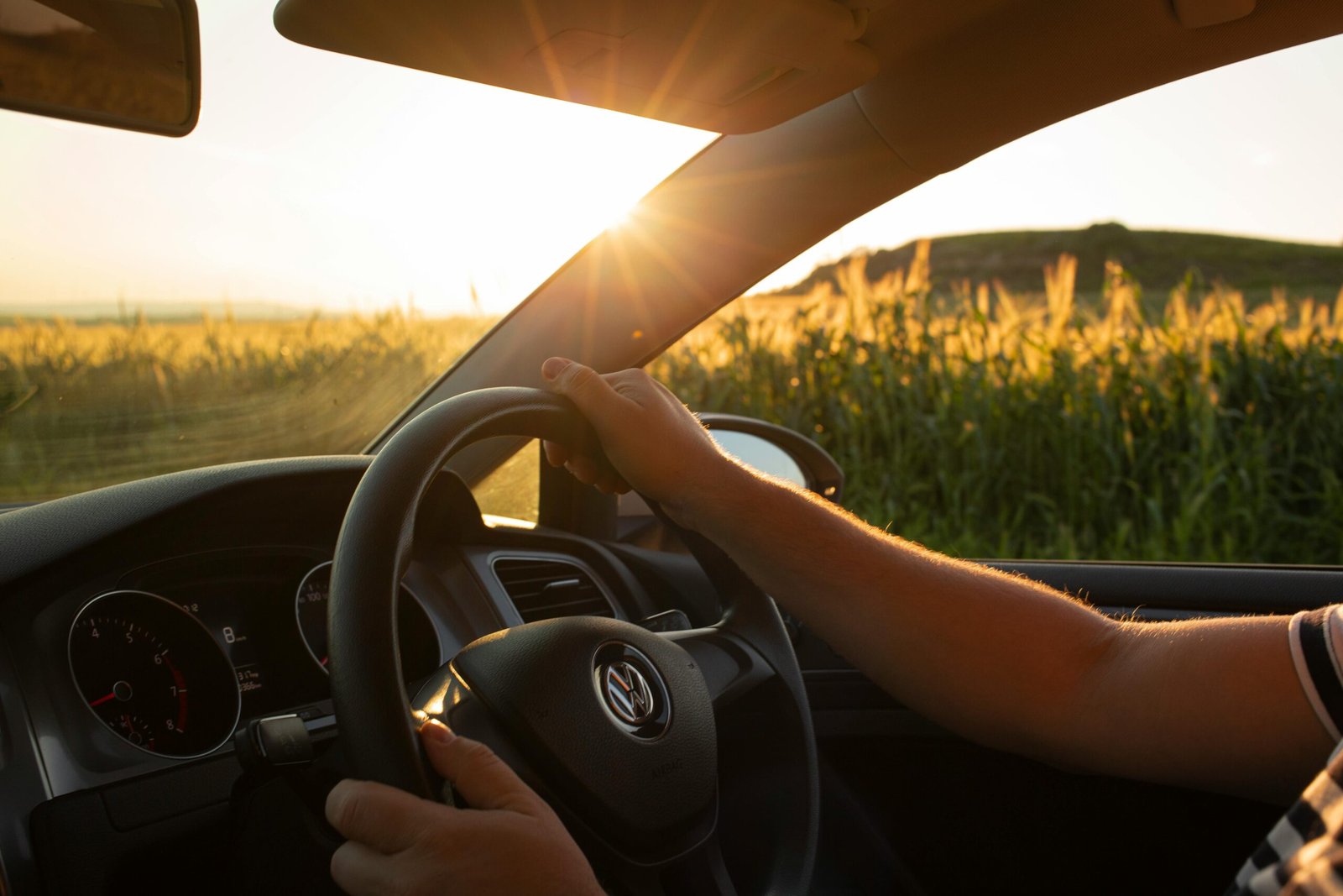 A driver's view of a countryside road at sunset, focusing on the steering wheel.